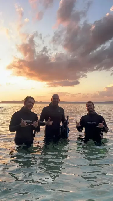 Three divers standing in the water beneath a sunset sky